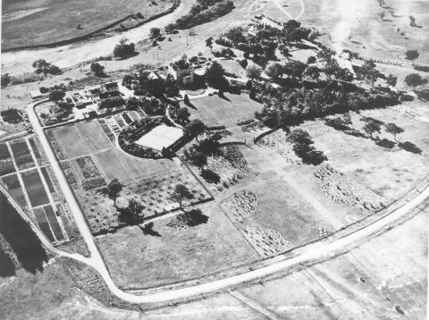 a black and white photograph taken from an airpliane showing buildings, gardens and roads